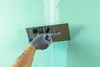 A person's hand wearing a gray glove is applying a green substance to a wall with a trowel. Produktbild-Vorschau