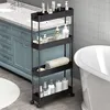 A slim, black, four-tier rolling storage cart filled with various bathroom products and towels, placed next to a bathtub and a blue vanity in a bathroom. Produktbild-Vorschau
