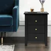 A black nightstand with three drawers is placed next to a blue velvet armchair. A glass of amber liquid and a vase with lavender are on top of the nightstand. Podgląd zdjęcia produktu