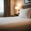 A close-up view of a neatly made hotel bed with white striped bedding and a large white pillow. Produktbild-Vorschau