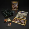 A collection of board game components, including miniatures, cards, a quest book, and a game box, laid out on a dark surface. Produktbild-Vorschau
