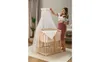 A pregnant woman is standing next to a crib, adjusting a canopy. Produktbild-Vorschau