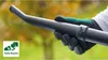 A gloved hand holding a black leaf blower nozzle with a green and white graphic overlay. Produktbild-Vorschau