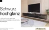 A modern living room scene featuring a black high-gloss TV lowboard mounted on a wall, with a large TV above it. A coffee table with a vase and a rug are in the foreground. Produktbild-Vorschau