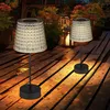 Two solar table lamps on a wooden deck at dusk, with plants and lanterns in the background. Produktbild-Vorschau
