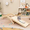 A young child is playing on a wooden climbing structure with a slide in a playroom. Produktbild-Vorschau