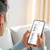 A person is holding a smartphone and wearing an earbud, interacting with an app that displays audio settings. Anteprima dell’immagine prodotto