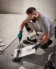 A man is kneeling on the floor, using a tile cutter to cut a tile. Produktbild-Vorschau