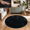 A round black rug in a living room setting, with a sofa and a cabinet in the background. Produktbild-Vorschau