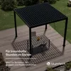 A black pergola with a slatted roof is set up on a wooden deck next to a table and chairs. The scene is set in a garden with grass and bushes in the background. Produktbild-Vorschau