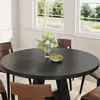 A round black dining table with a bouquet of flowers and a bowl of fruit in the center, surrounded by brown chairs, in a room with large windows overlooking a garden. Anteprima dell’immagine prodotto