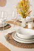 A dining table setting with white ceramic dishes, wine glasses, and a bouquet of yellow flowers. Voir les images du produit