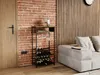 A wine rack filled with bottles and glasses stands next to a brick wall and a sofa in a living room. Podgląd zdjęcia produktu