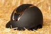 A black riding helmet with rose gold and glitter accents rests on a bed of straw. Produktbild-Vorschau