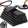 A pile of black hot glue sticks with a hand holding one in the background and a close-up of melted glue being dispensed. Voir les images du produit