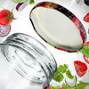 A glass jar lid with a fruit pattern and the rim of a glass jar are shown against a white background, surrounded by floating ingredients like tomatoes, cucumber, and lettuce. Podgląd zdjęcia produktu