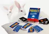 A board game box and cards are arranged on a pillow, with two white rabbits in the background. Podgląd zdjęcia produktu