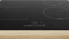 A close-up view of a black induction hob set into a wooden countertop. Voir les images du produit