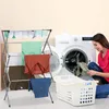A woman is folding laundry next to a washing machine and a drying rack. Produktbild-Vorschau