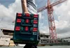 A person carrying a stack of Metabo toolboxes on a construction site with a crane in the background. Produktbild-Vorschau