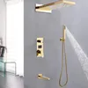 A modern gold shower system mounted on a gray wall, with water flowing from the showerhead and handheld sprayer. Podgląd zdjęcia produktu