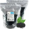 Two sealed plastic bags of activated charcoal pellets, with a label on one bag, and a pile of pellets with green leaves in the foreground. Anteprima dell’immagine prodotto