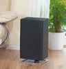 A black air purifier sits on a wooden floor next to a chair and a plant. Podgląd zdjęcia produktu