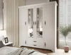 A white wardrobe with mirrored doors is shown in a bedroom setting, next to a nightstand with a lamp and a framed picture. Produktbild-Vorschau