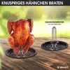 A roasted chicken is displayed on a roasting rack with a drip pan, next to another roasting rack and drip pan. The background is a blurred outdoor scene with greenery and a wooden table. Produktbild-Vorschau