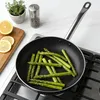 Asparagus being cooked in a frying pan on a stovetop, with lemons and a herb plant in the background. Produktbild-Vorschau