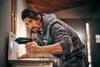 A man is using a cordless drill to attach something to a wall. Produktbild-Vorschau