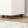 Close-up of the bottom of a white cabinet with black wheels on a wooden floor. Produktbild-Vorschau