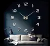 A large, modern wall clock with 3D numbers is mounted on a dark blue wall above a sofa. A lamp is positioned to the left of the sofa. Produktbild-Vorschau
