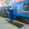A worker in a blue uniform stands on an anti-fatigue mat in front of a large industrial machine. Produktbild-Vorschau