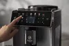 A hand touching the touchscreen of a coffee machine. Produktbild-Vorschau