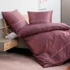 A neatly made bed with patterned bedding and pillows, next to a nightstand with a small vase. Produktbild-Vorschau