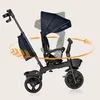 A dark navy blue Lionelo Kori tricycle is shown against a light beige background, with orange arrows indicating rotational movement of the seat and handle. Podgląd zdjęcia produktu