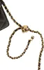 A close-up of a black quilted handbag strap with a gold chain and a gold charm. Produktbild-Vorschau