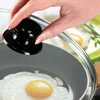 A hand is holding a black lid handle over a frying pan with a fried egg. Podgląd zdjęcia produktu