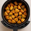 A close-up view of roasted potato wedges with rosemary sprigs in an air fryer basket. Produktbild-Vorschau