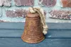 A rusty bell with a rope hangs in front of a brick wall and a wooden surface. Anteprima dell’immagine prodotto