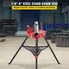 A red and black steel stand chain vise with a pipe clamped in it, set in a workshop environment. Náhled obrázku produktu