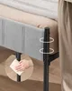 A close-up of a gray upholstered bed frame with black metal legs and a beige blanket on top. A hand is shown cleaning one of the legs with a cloth. Náhled obrázku produktu