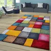 A colorful geometric rug is placed on a wooden floor in a living room setting, with a sofa and chair in the background. Produktbild-Vorschau