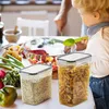 A child and an adult in a kitchen setting with food items and storage containers. Produktbild-Vorschau
