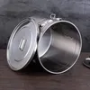 A stainless steel canister with its lid open, placed on a wooden surface with a gray textured background. Produktbild-Vorschau