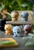 A collection of small, spring-loaded animal figurines are arranged on a surface with a blurred background of plants and wooden shelves. Produktbild-Vorschau