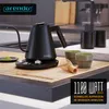 A black electric kettle with a gooseneck spout sits on a charging base on a kitchen counter, next to matcha tea cups and a whisk. A small pile of matcha powder is visible on a saucer. Produktbild-Vorschau