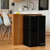 A black dual-compartment trash can is shown next to a wooden kitchen island with chairs. Produktbild-Vorschau