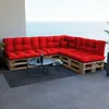 A sectional sofa made of wooden pallets with red cushions sits on a balcony overlooking the ocean. Produktbild-Vorschau